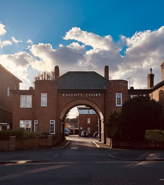 A view of the Knights Court entrance, featuring a traditional brick archway with the name displayed on a rectangular sign. The brickwork is reddish-brown with a textured surface, and the arch is toppe